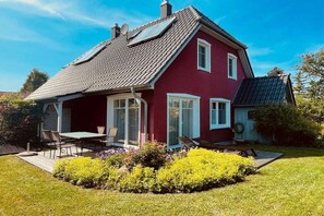 A red house with a sloped roof, a patio with a table and chairs, and a well-maintained garden. - Wiecker Landhus | FHH 1 (Wieck)