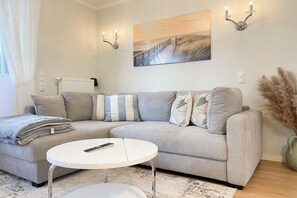 A modern living room with a grey sofa, a round coffee table, and a painting on the wall. - Holiday apartment with 1 bedroom (Timmendorfer Strand)