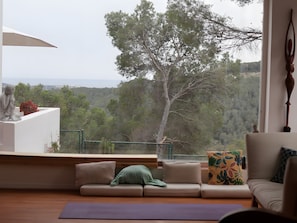 A room with a view of a tree and landscape, a sofa, a meditation mat, and a statue. - Villa Bohemia: Sea View, Private Pool, and Wi-Fi (Olivella)