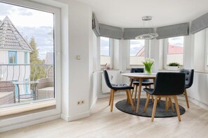 Un coin repas avec une table ronde, des chaises noires et une vue sur une maison, visible à travers une grande fenêtre.