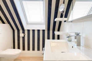 Une salle de bain moderne avec un puits de lumière, des toilettes blanches et un grand lavabo avec un miroir.