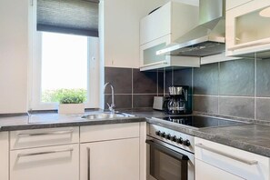A modern kitchen with a window, stainless steel appliances, and a tiled backsplash. - Holiday apartment with 1 bedroom (Timmendorfer Strand)