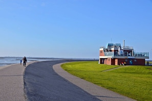 A coastal walkway with a building that appears to be a lifeguard station, featuring a fenced area and a viewing platform. - Holiday apartment with 2 bedrooms (Norden-Norddeich)