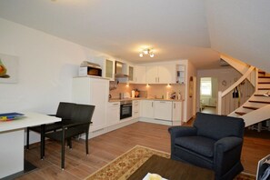A compact living space with a kitchenette, a dining area, and a staircase leading to another level. - Holiday apartment with 2 bedrooms (Norden-Norddeich)