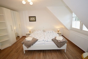 A bedroom with a sloped ceiling, a bed with a patterned duvet, bedside lamps, and a framed picture on the wall. - Holiday apartment with 2 bedrooms (Norden-Norddeich)
