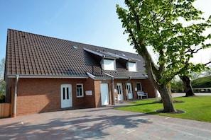 A two-story brick building with a tiled roof, a covered driveway, and a well-maintained lawn. - Holiday apartment with 2 bedrooms (Norden-Norddeich)