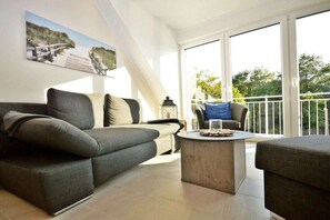 A modern living room with a sofa, a coffee table, and a balcony with a railing. - Holiday apartment with 1 bedroom (Norddeich)