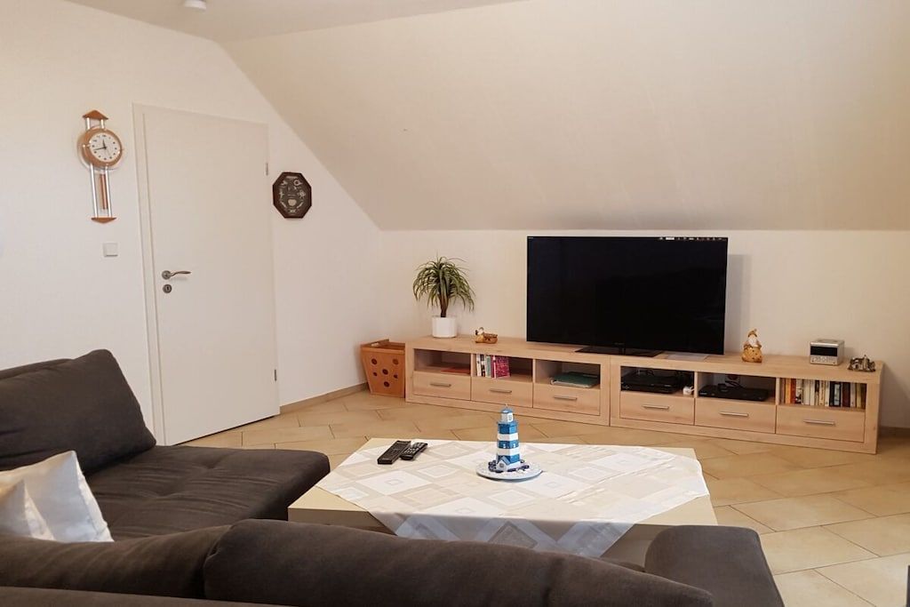 A living room with a flat-screen TV, a coffee table with a decorative item, a sofa, and a cabinet with books and decorative objects.