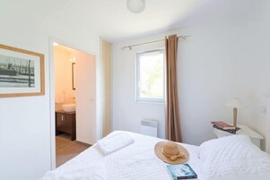 A bedroom with a bed, a window with curtains, a bedside table with a lamp, and a framed picture on the wall.