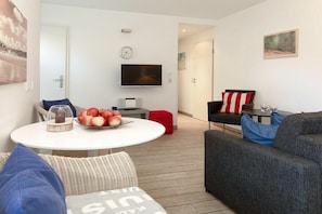 A modern living room with a round table, a sofa, a TV, and a red suitcase. - Holiday apartment in Juist with swimming pool (Juist)