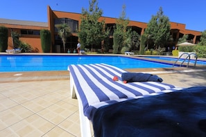 Zona de piscina amb una cadira relaxant i una tovallola, un edifici al fons i un cel serè.
