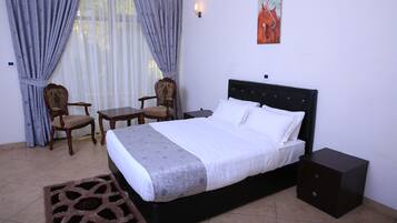 A bedroom with a bed, two chairs, a small table, a nightstand, and a rug.