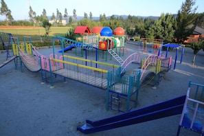 Un parc infantil amb diverses estructures de joc, incloent tobogans, cadenes i zones d'escalada.