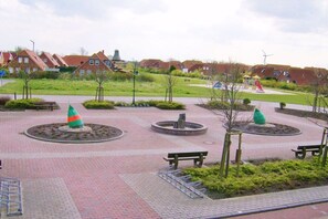 Ein Wohngebiet mit Häusern, einem Spielplatz und einem gepflasterten Platz mit Bänken und Poller.