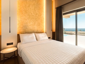 A hotel room with a large bed, a small table, and a view of the sea through large windows. - Villa in Ierapetra With Swimming Pool (Ierapetra)