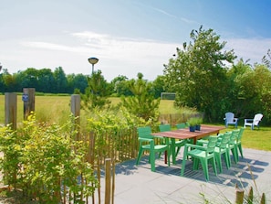 Eine Terrass mit Holztisch und grünen Stühlen, umgeben von einem Holzzaun und viel Grün.
