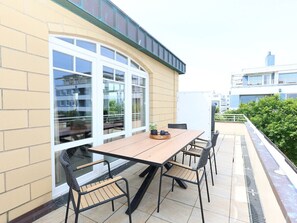 A patio with a wooden table and chairs, a glass door, and a view of the city. - 28 Residence Bismarck (Sylt)
