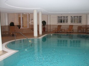 An indoor swimming pool with a clear water surface, surrounded by lounge chairs and potted plants. - 28 Residence Bismarck (Sylt)