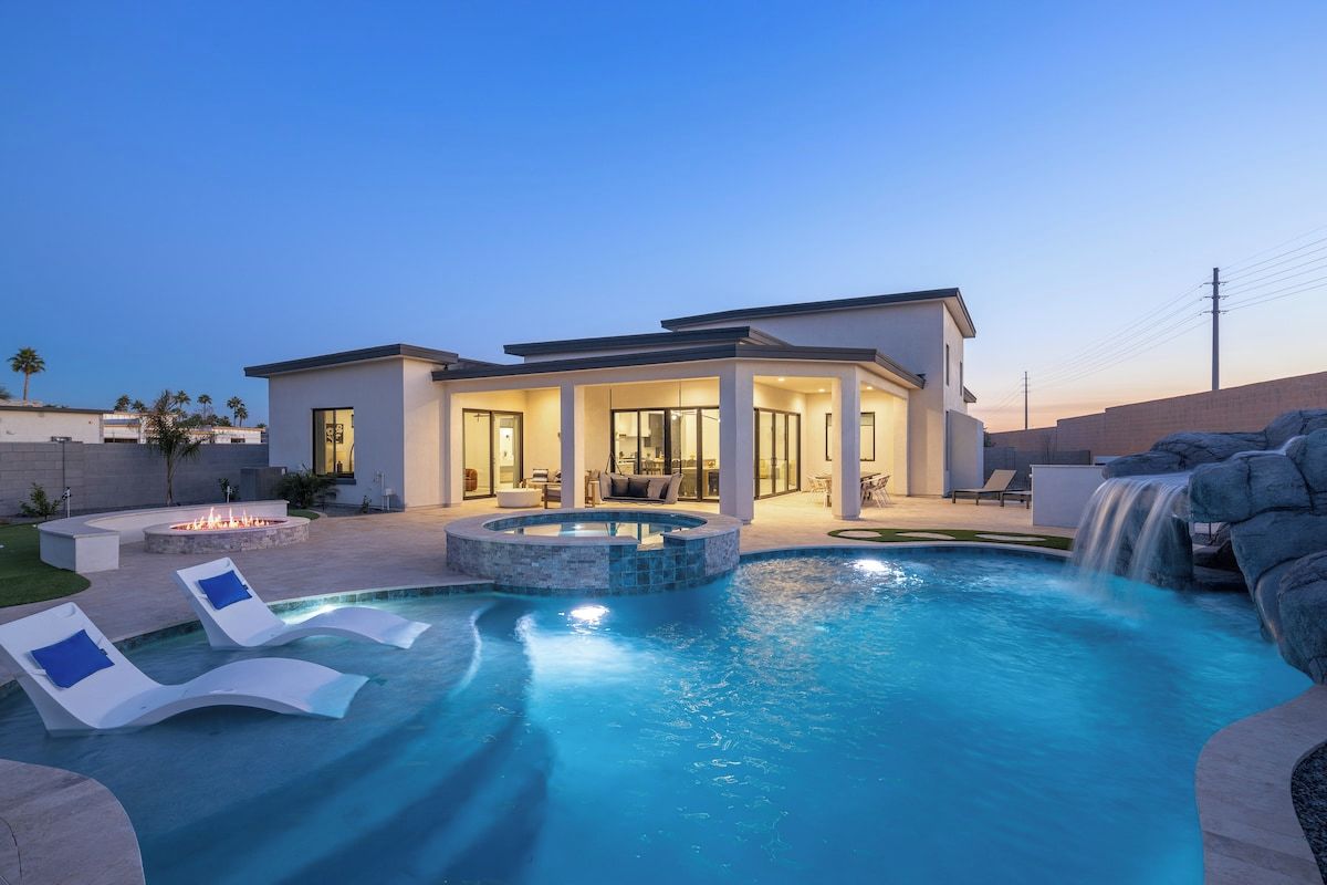 A modern house with a swimming pool, lounge chairs, and a waterfall feature.