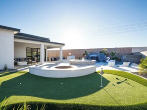 Ein modernes Haus mit Swimmingpool, einer runden Terrasse und einem gepflegten Rasen.