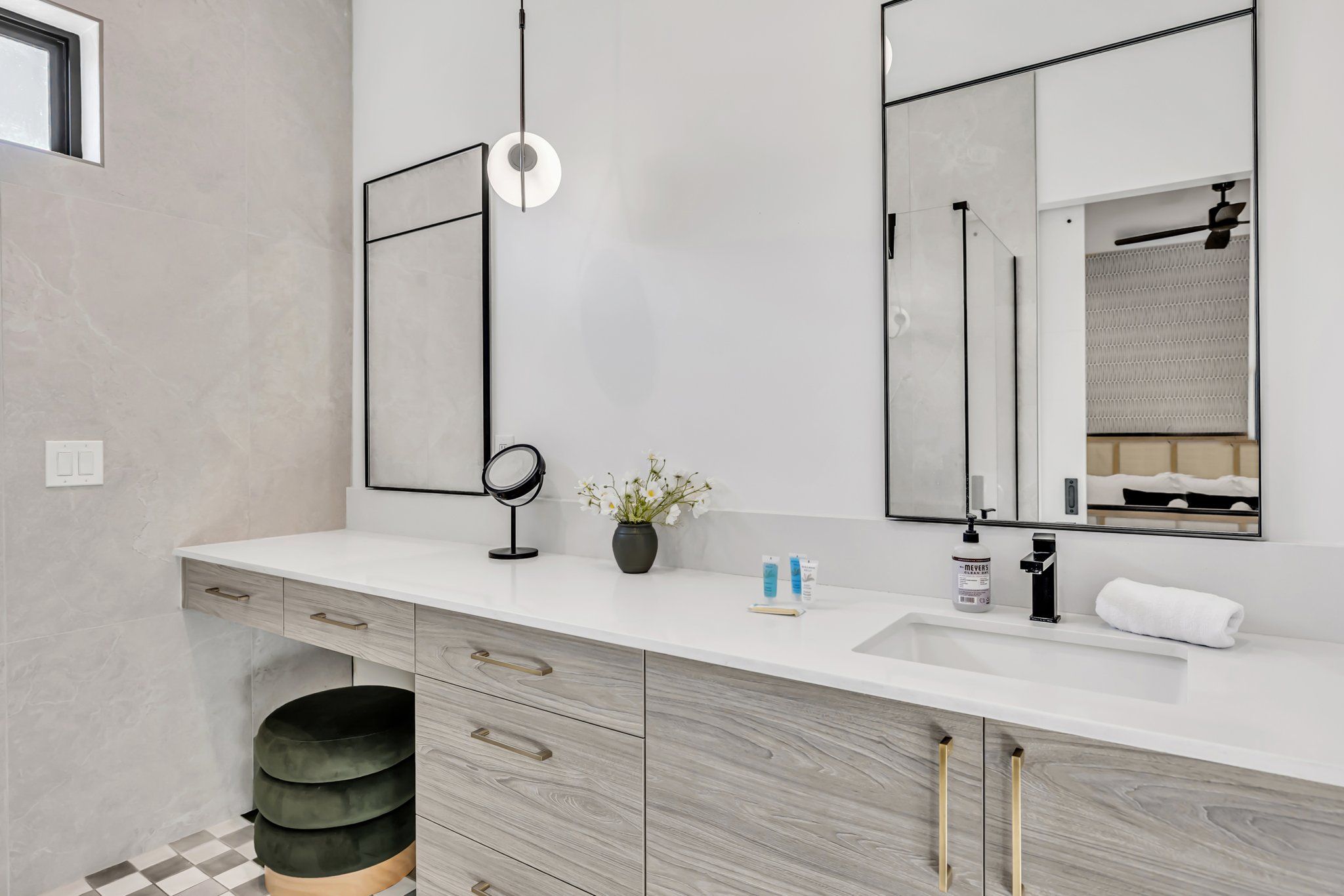 A modern bathroom with a white vanity, a large mirror, a round mirror, and a small potted plant.