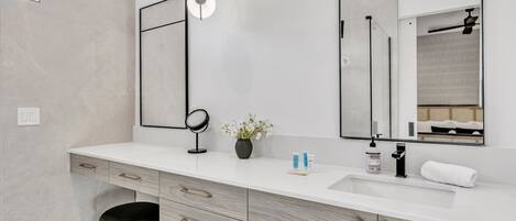 A modern bathroom with a white vanity, a large mirror, a round mirror, and a small potted plant.
