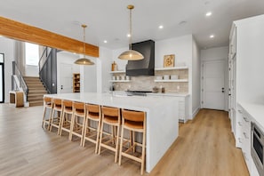 A modern kitchen with a central island, bar stools, pendant lighting, and a staircase leading to an upper level. - Modern Manor-6BR, Pool&Spa, Air Hockey, Ping Pong (Scottsdale)