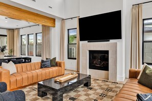 A modern living room with a leather sofa, a glass coffee table, a flat-screen TV, and a fireplace. - Modern Manor-6BR, Pool&Spa, Air Hockey, Ping Pong (Scottsdale)