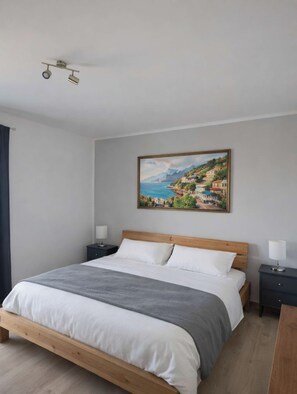 Une chambre à coucher avec un lit en bois, du linge de lit blanc, un tableau représentant une ville côtière et deux tables de chevet avec des lampes.
