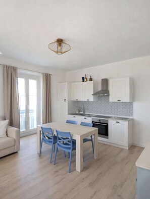 Een moderne keuken met witte kastjes, een centraal eiland en een eethoek met blauwe stoelen.
