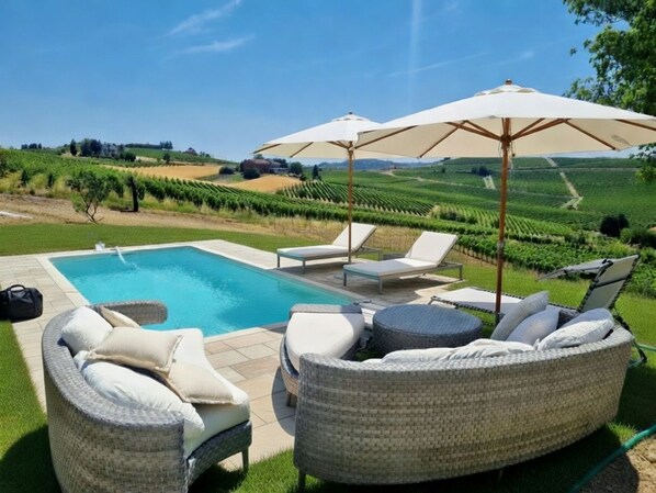 Un espace piscine agrémenté de chaises longues et de parasols, entouré d’un jardin aménagé et d’un vignoble.