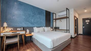 A modern hotel room with a large bed, a desk with a chair, a wardrobe, and an air conditioning unit.
