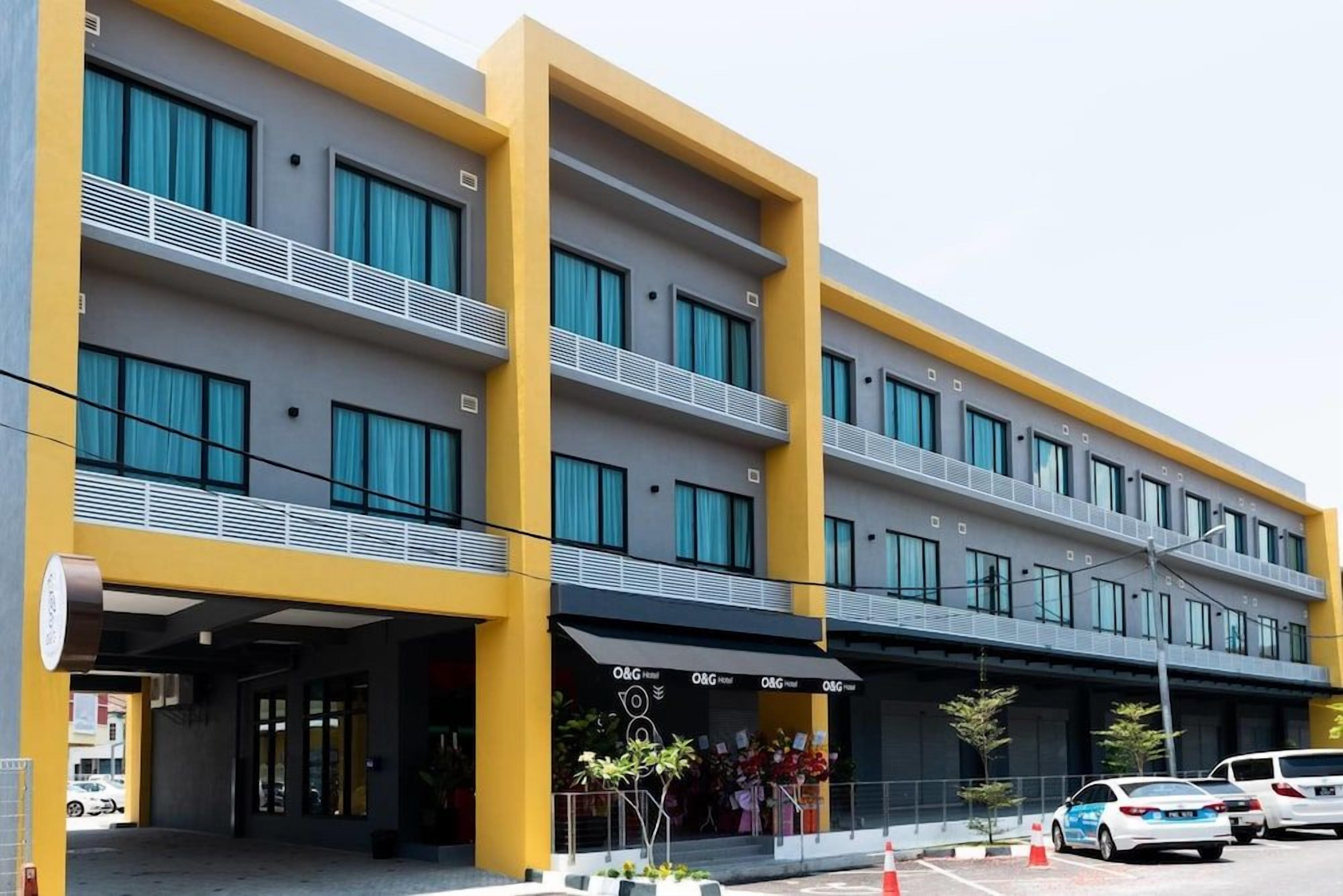 A multi-story hotel with a yellow and grey facade, balconies with white railings, and a storefront with the hotel name.