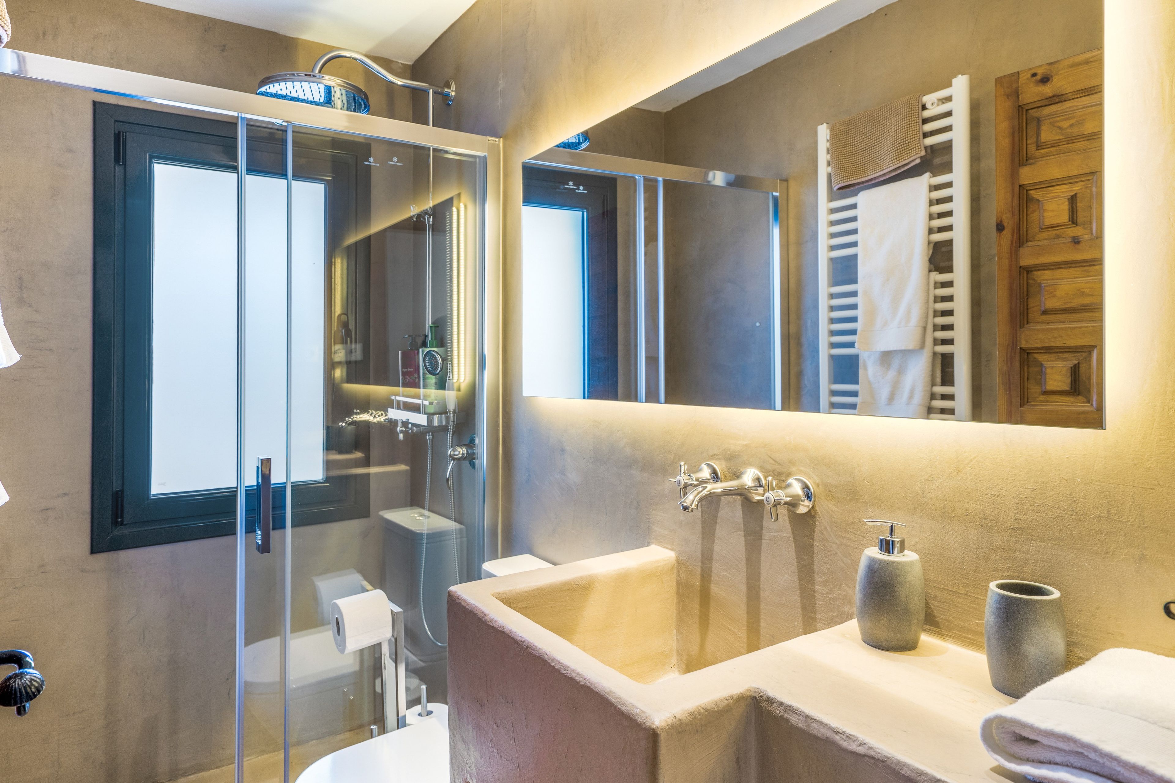 Un baño moderno con ducha envuelta en vidrio, un espejo grande y un lavabo con toallero.