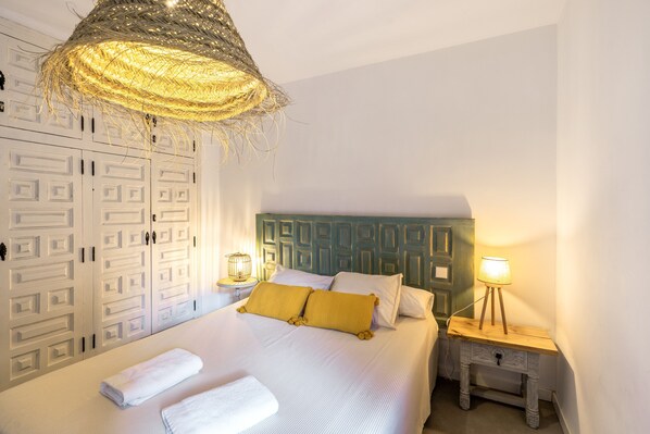 A bedroom with a bed, a bedside table with a lamp, a hanging light fixture, and a wardrobe with patterned doors.