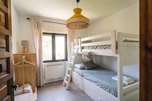 Un dormitorio con una cama litera, un armario de madera, un radiador, una ventana con cortinas y una lámpara colgante.