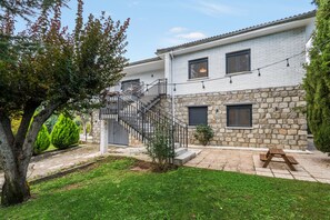 Un edificio de dos pisos con fachada de piedra, una escalera con barandillas de metal y un pequeño jardín con una mesa de picnic.