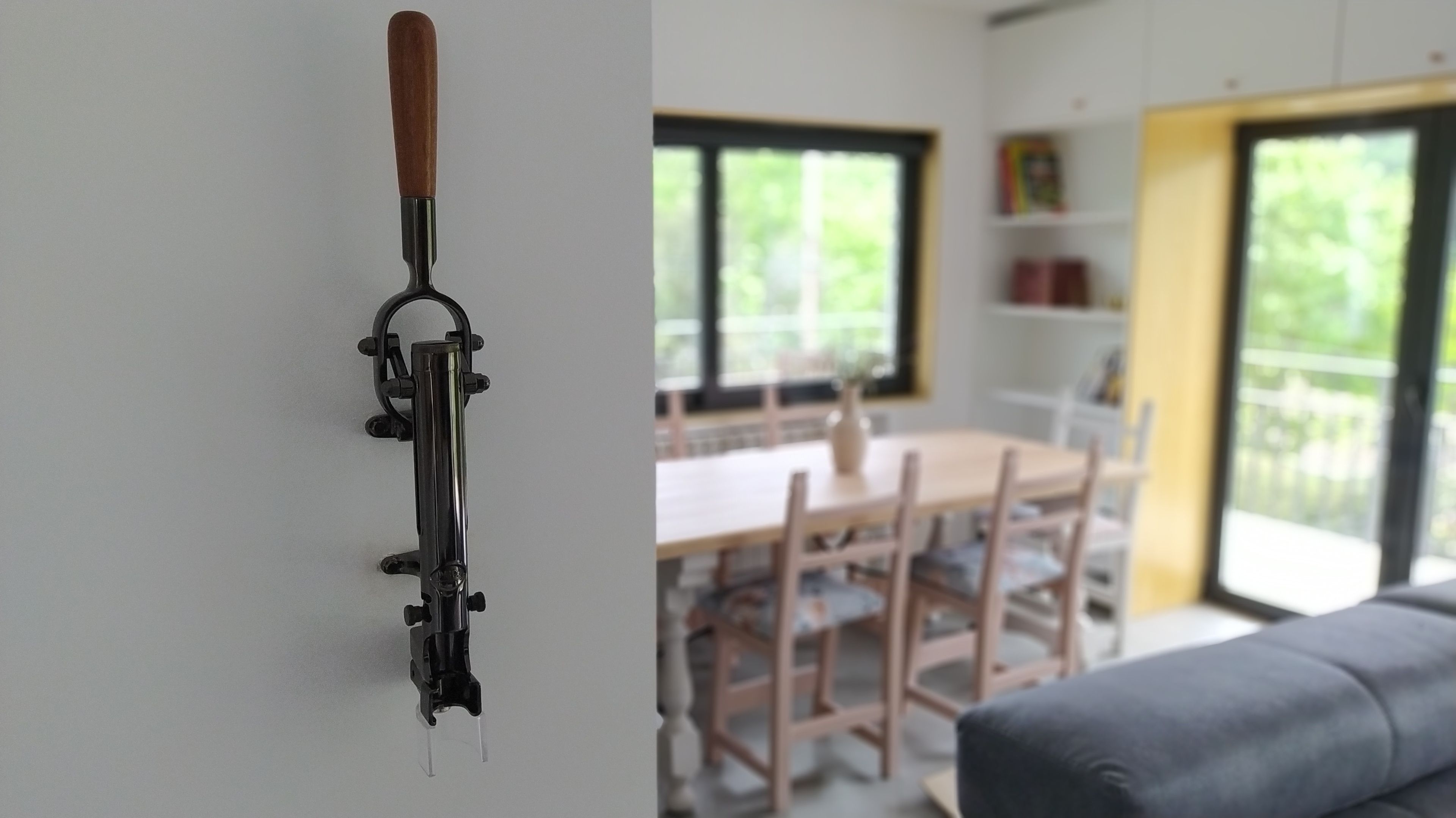 Een keuken met een houten tafel en stoelen, een raam met uitzicht op groen, en een object aan de muur.