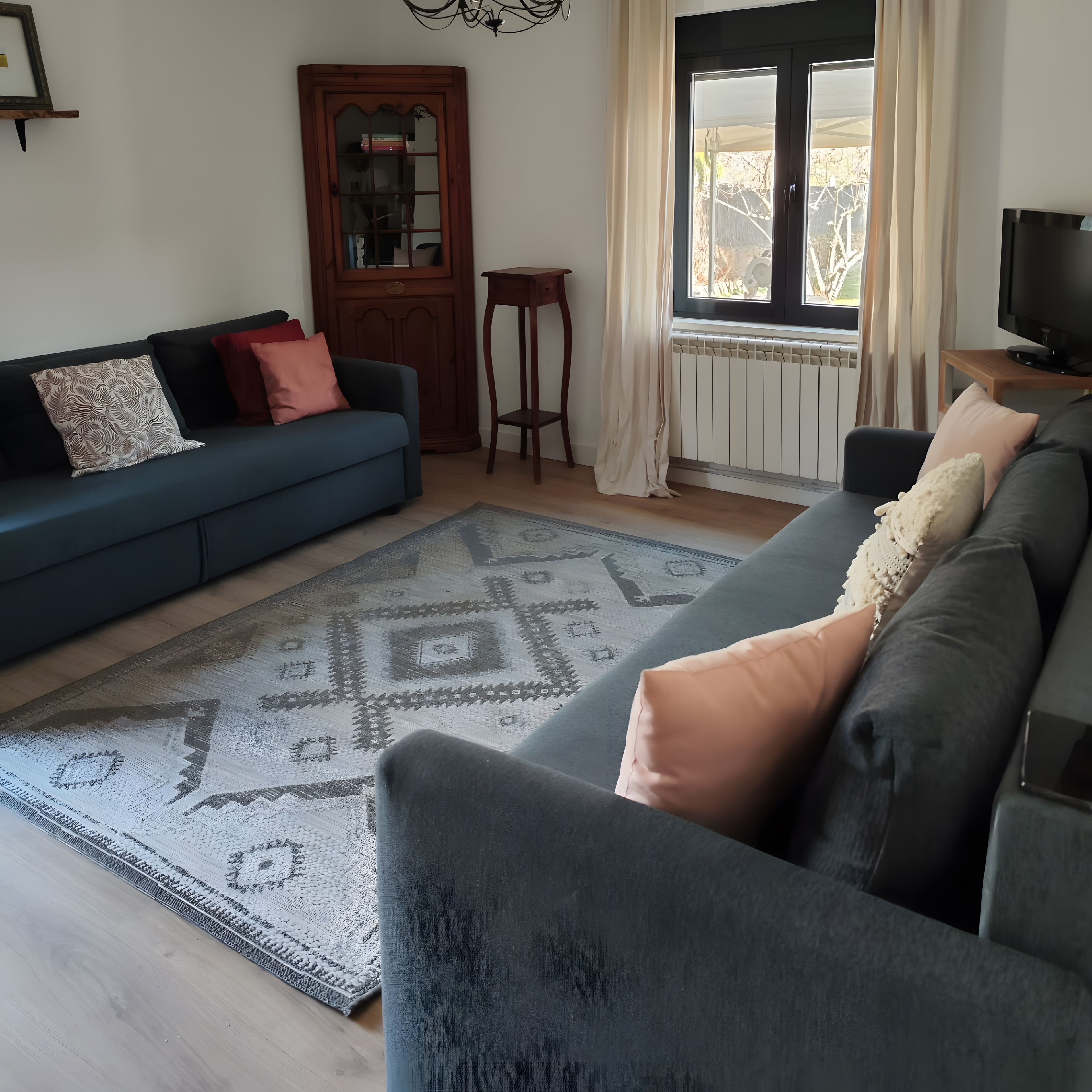 A living room with a blue sofa, a patterned rug, and a television on a stand.