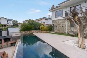 Una propiedad residencial con piscina, muros de piedra y un árbol.