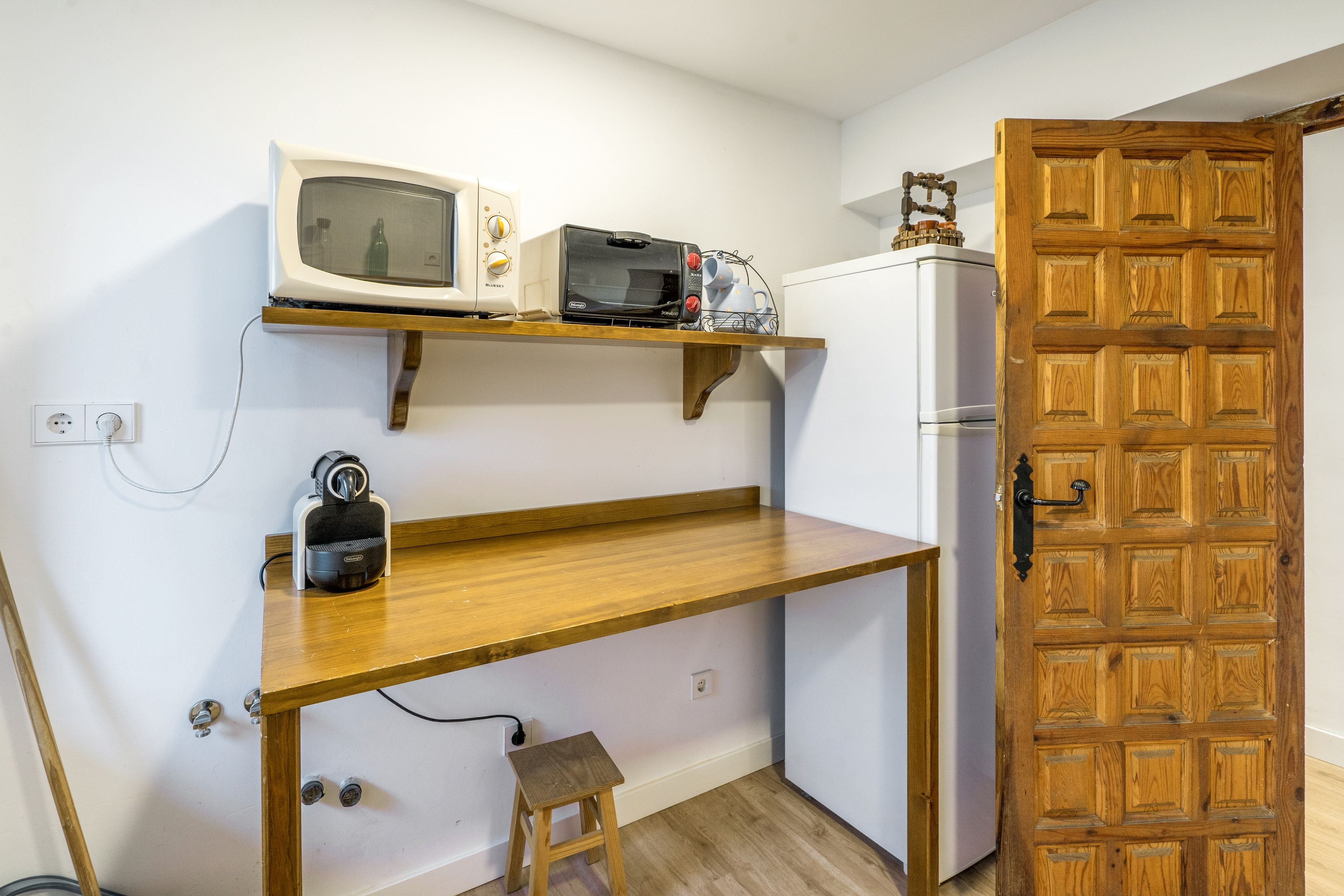 A compact kitchen with a wooden countertop, a microwave, a toaster, and a refrigerator.