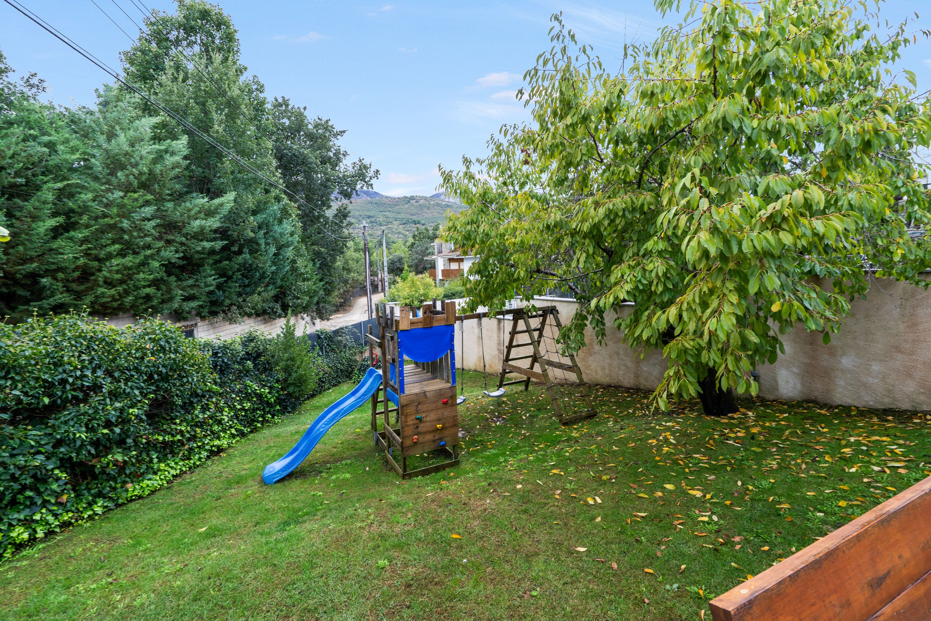 A backyard with a wooden play structure, a blue slide, and a tree.