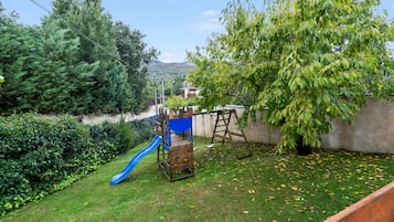 A backyard with a wooden play structure, a blue slide, and a tree.