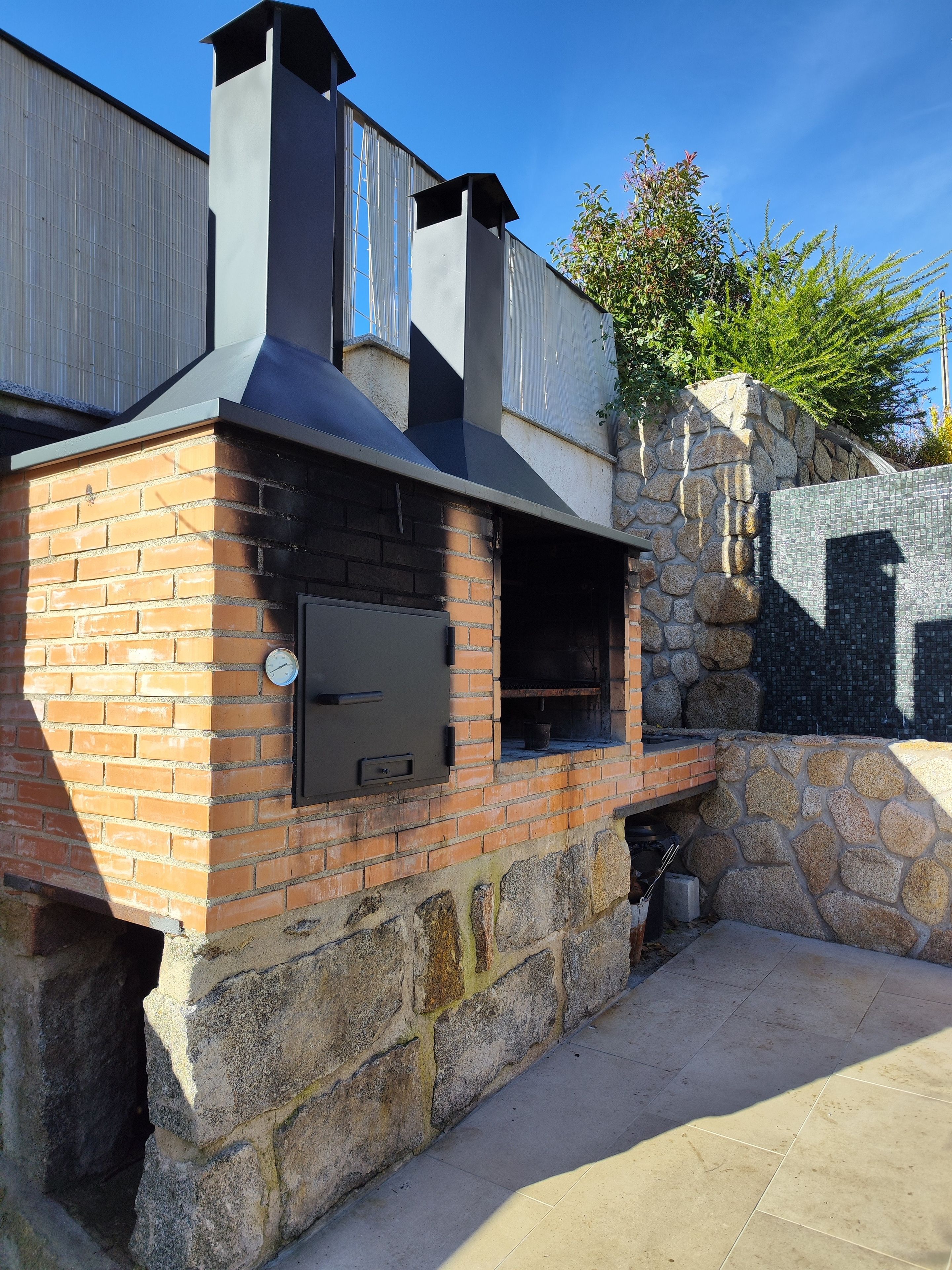 Un horno de ladrillo al aire libre con una pared de piedra y una chimenea de metal.