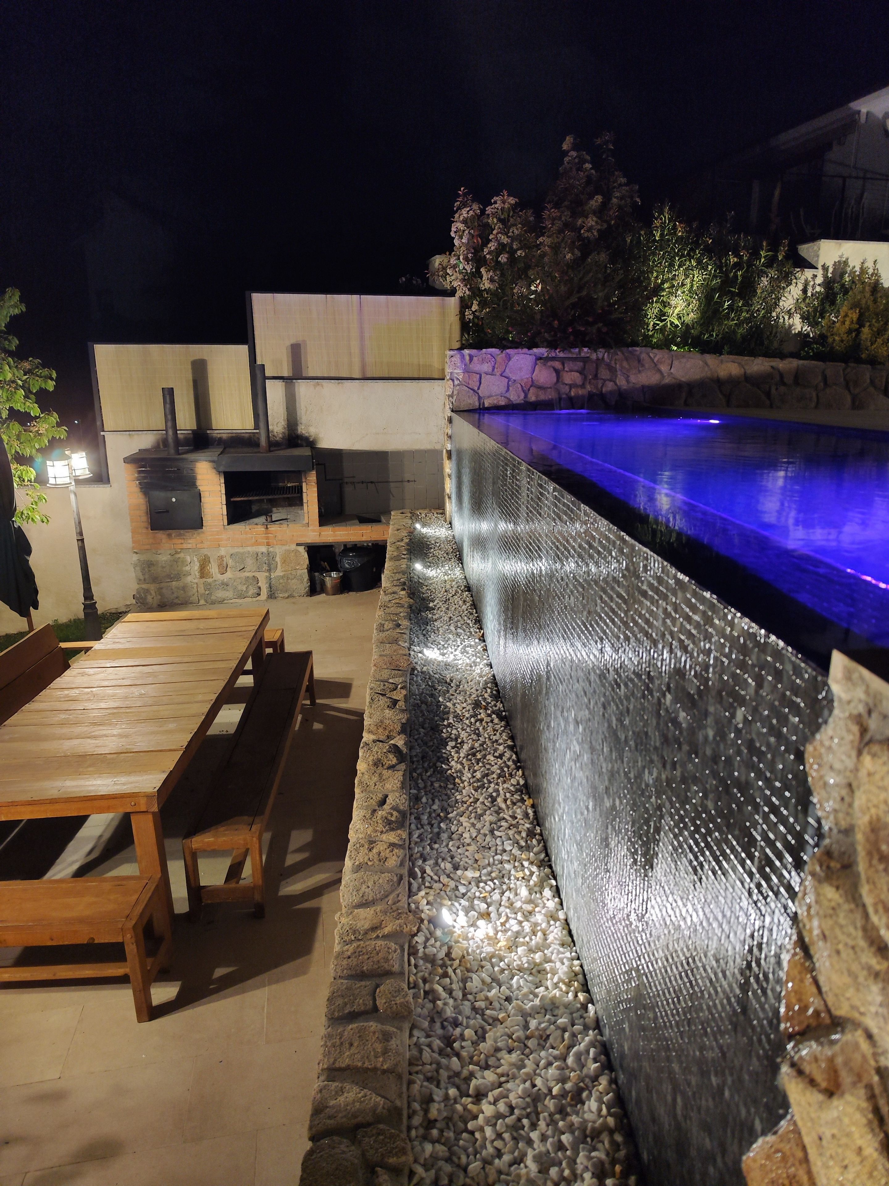 An outdoor patio with a pool, stone wall, and a barbecue area.