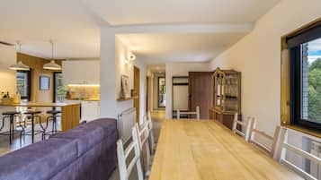 A modern kitchen with a bar area, a dining table with chairs, and a large window.