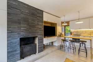 A modern kitchen with a stone fireplace, a large window, and bar stools.