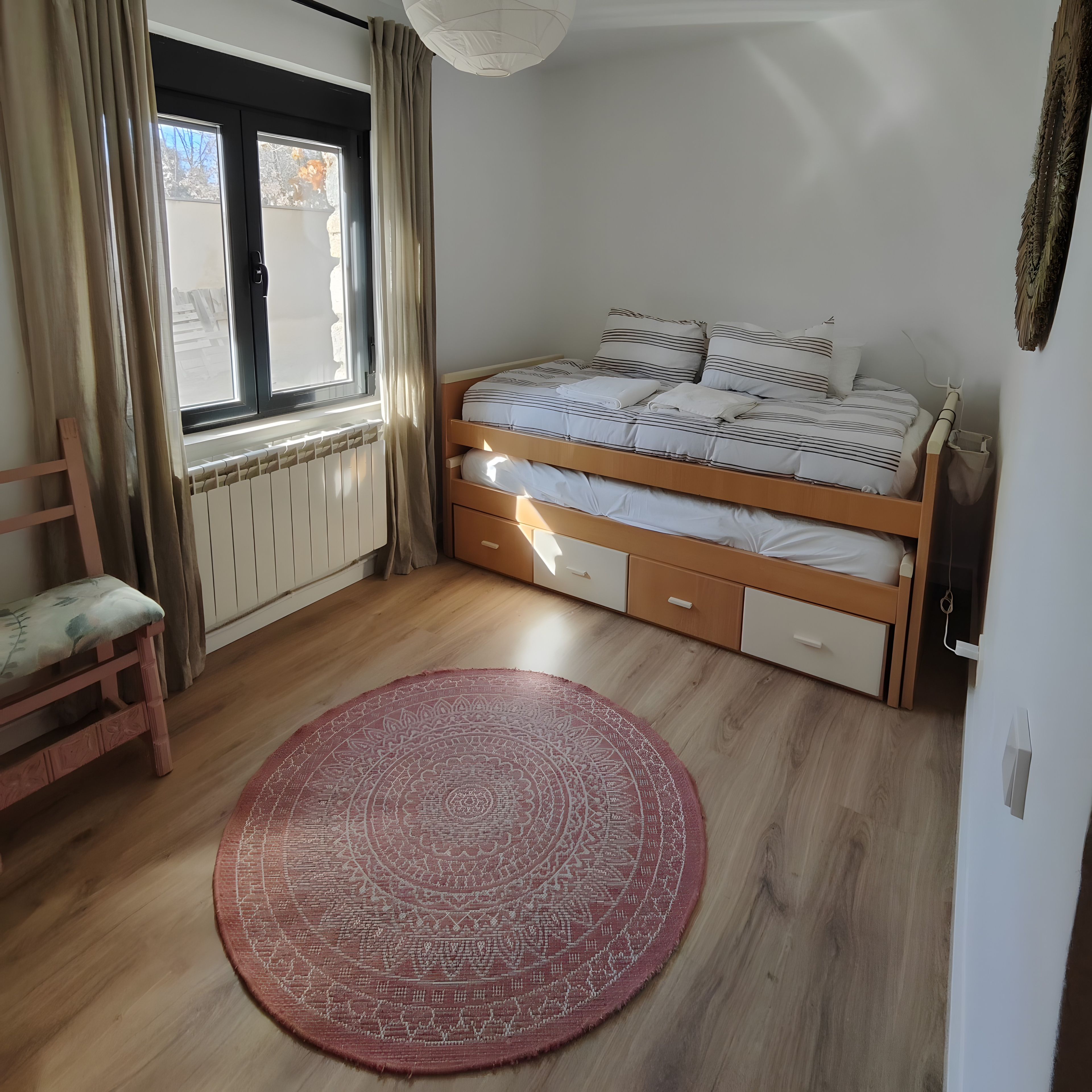 Un dormitorio con cama, ventana, radiador, suelo de madera y una alfombra roja.