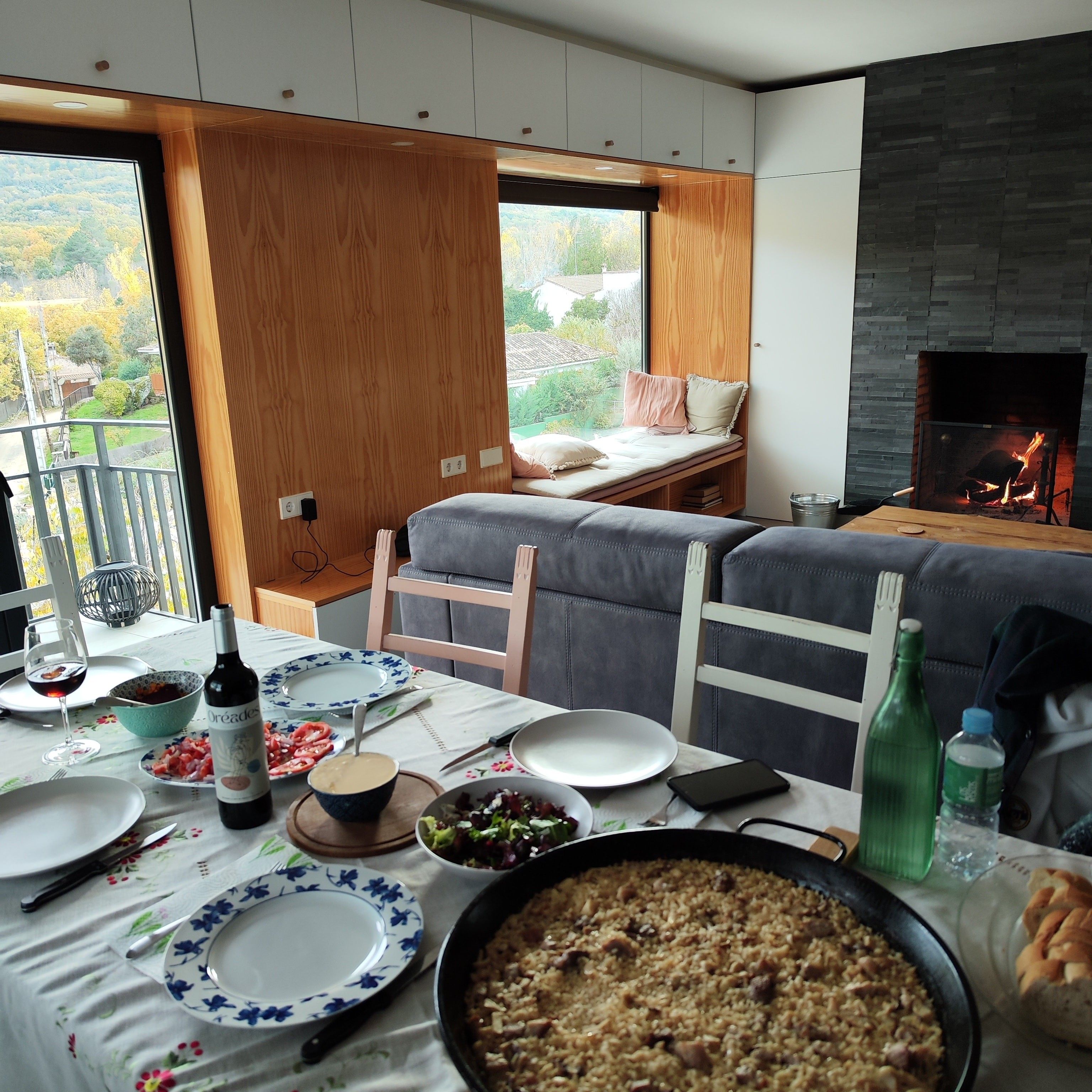 Un comedor con una mesa preparada para una comida, una olla de comida y vistas a un balcón con una cama y una chimenea.