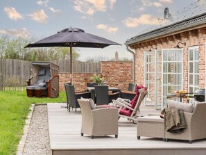 Eine Terrasse mit Gartenmöbeln, einem Grill und einem Backsteinhaus mit Fenstern.